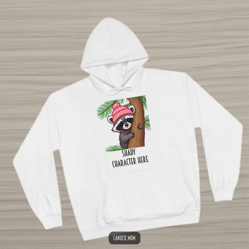 Funny Raccoon Hat Hoodie: A curious raccoon wearing a tiny knitted hat peeks out from behind a pine tree, looking intriguing.